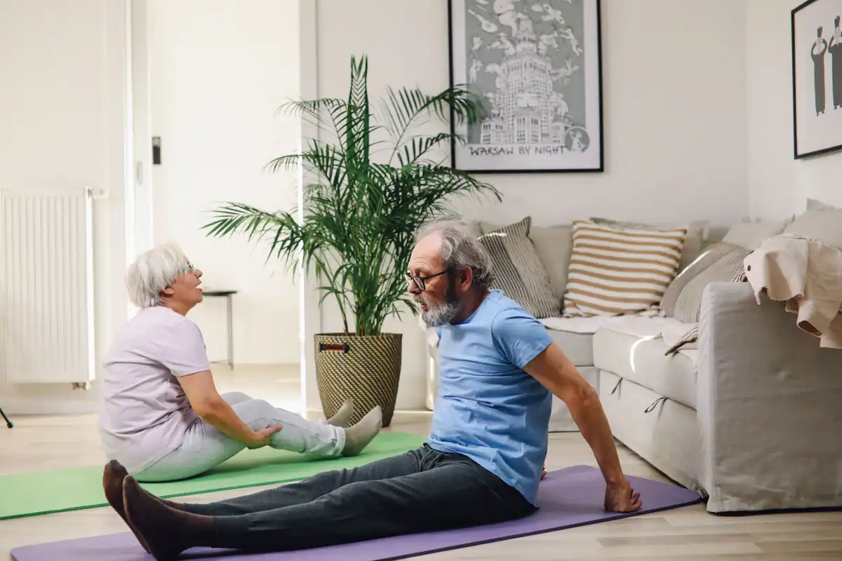 Un cuplu de seniori face exerciții pe saltele în sufragerie, la un antrenament lejer acasă