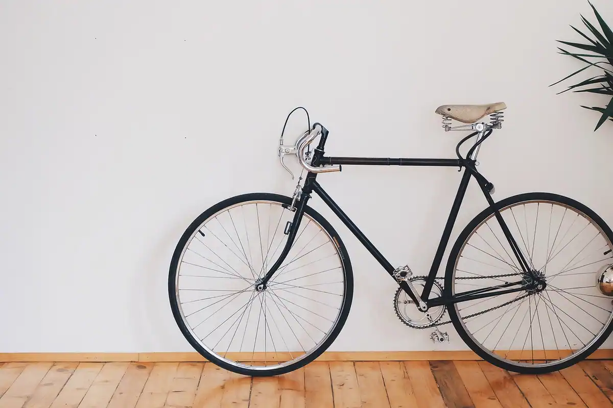 Bicicletă clasică neagră sprijinită de un perete alb, într-o încăpere cu parchet