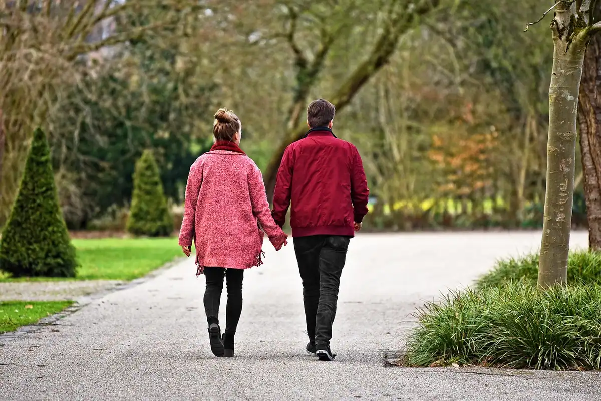 Cuplu de vârstă mijlocie merge de mână pe aleea unui parc, la un efort cardio blând