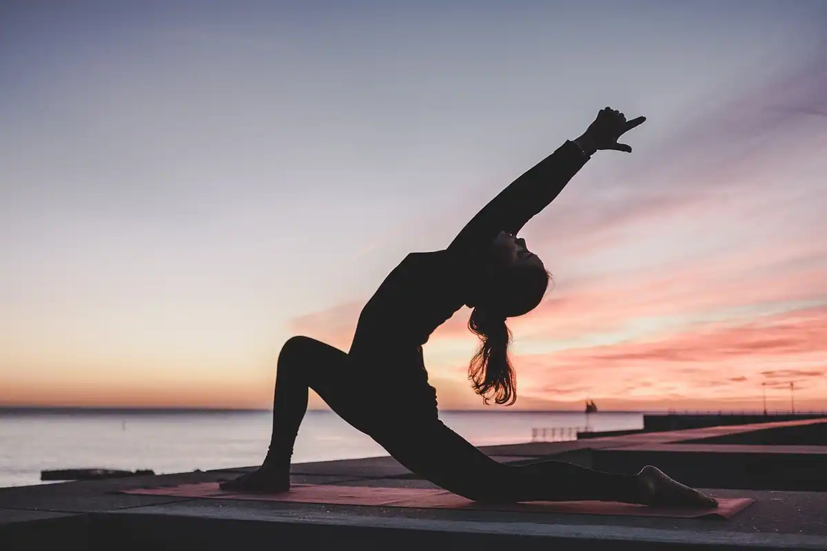 Siluetă de femeie într-o poziție de yoga la apus, pe o saltea, fără aparate