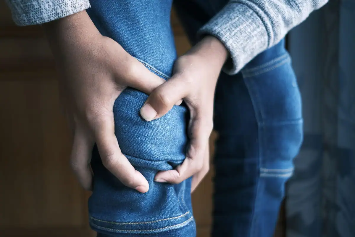 Două mâini strâng un genunchi dureros, semn de durere musculară după efort