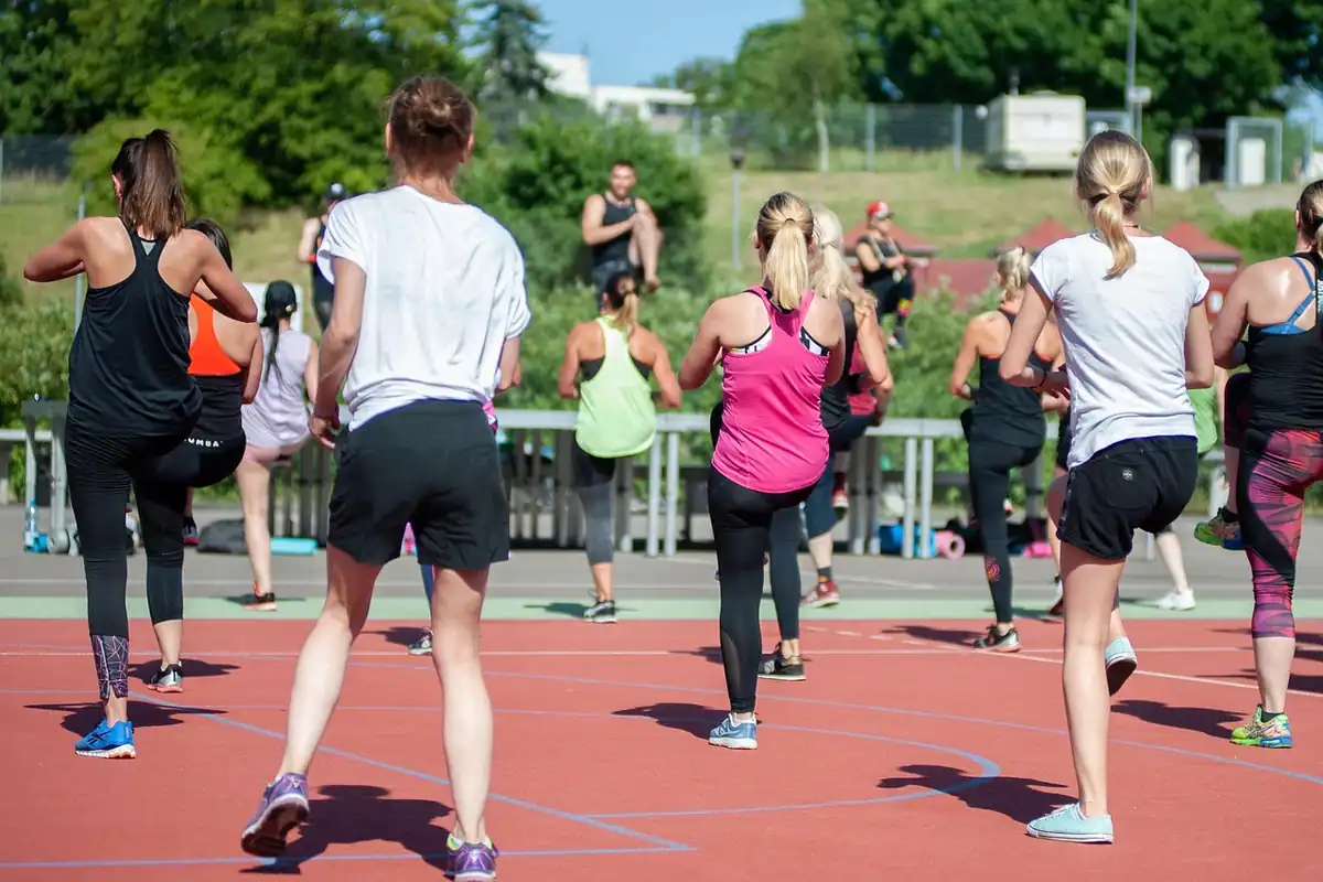 Grup de femei fac exerciții cardio în aer liber, pe un teren de sport