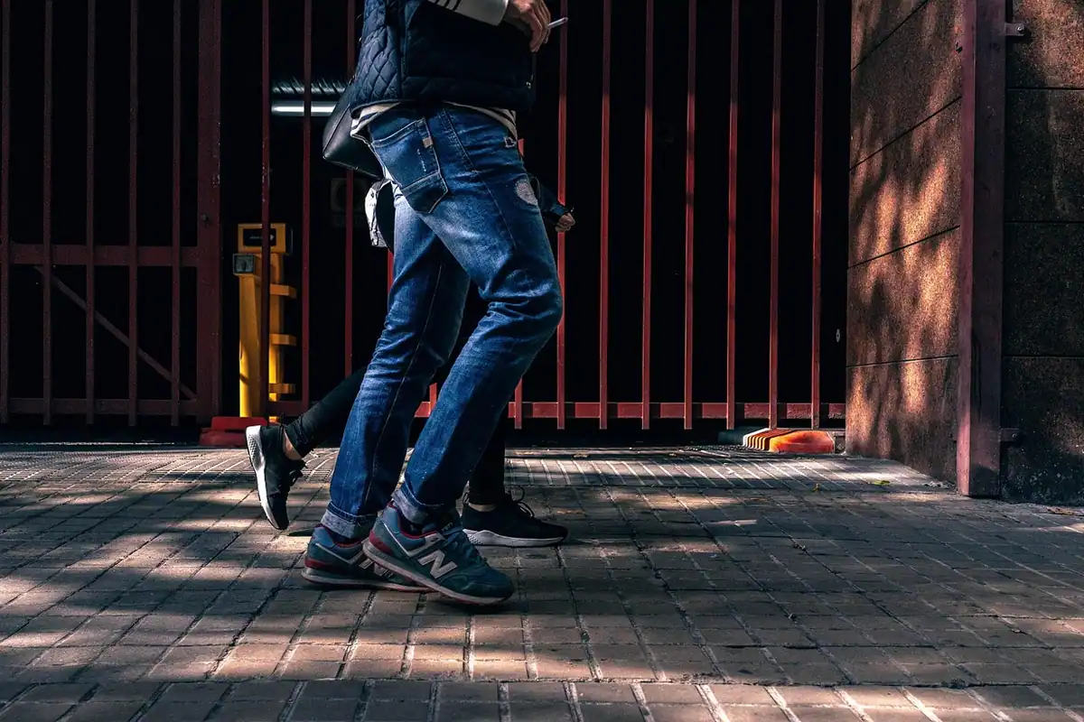 Picioare în blugi și adidași pășesc pe pavajul unei străzi, într-un mers alert