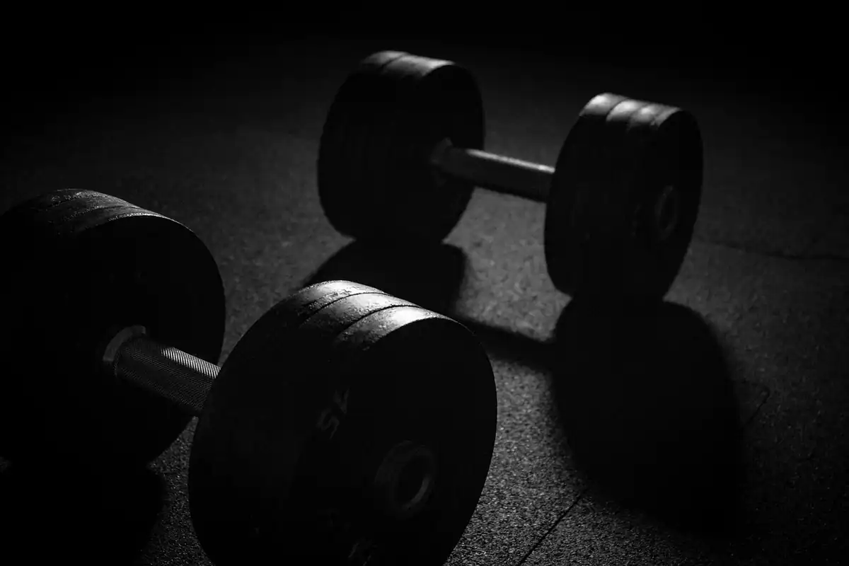 Gantere negre pe podeaua unei săli, într-o lumină slabă, între serii de exerciții