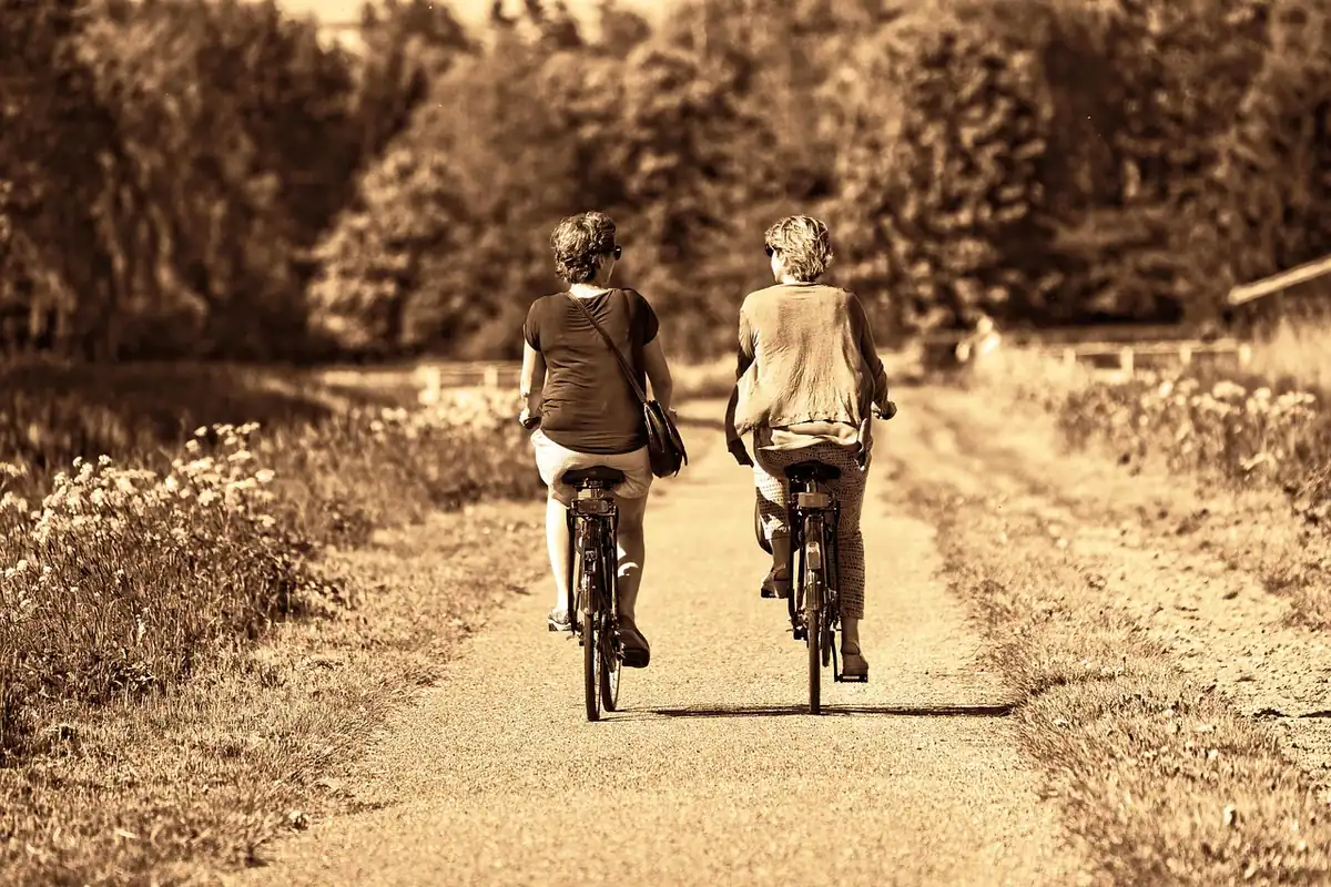 Două persoane merg pe biciclete pe un drum de țară, cu spatele drept